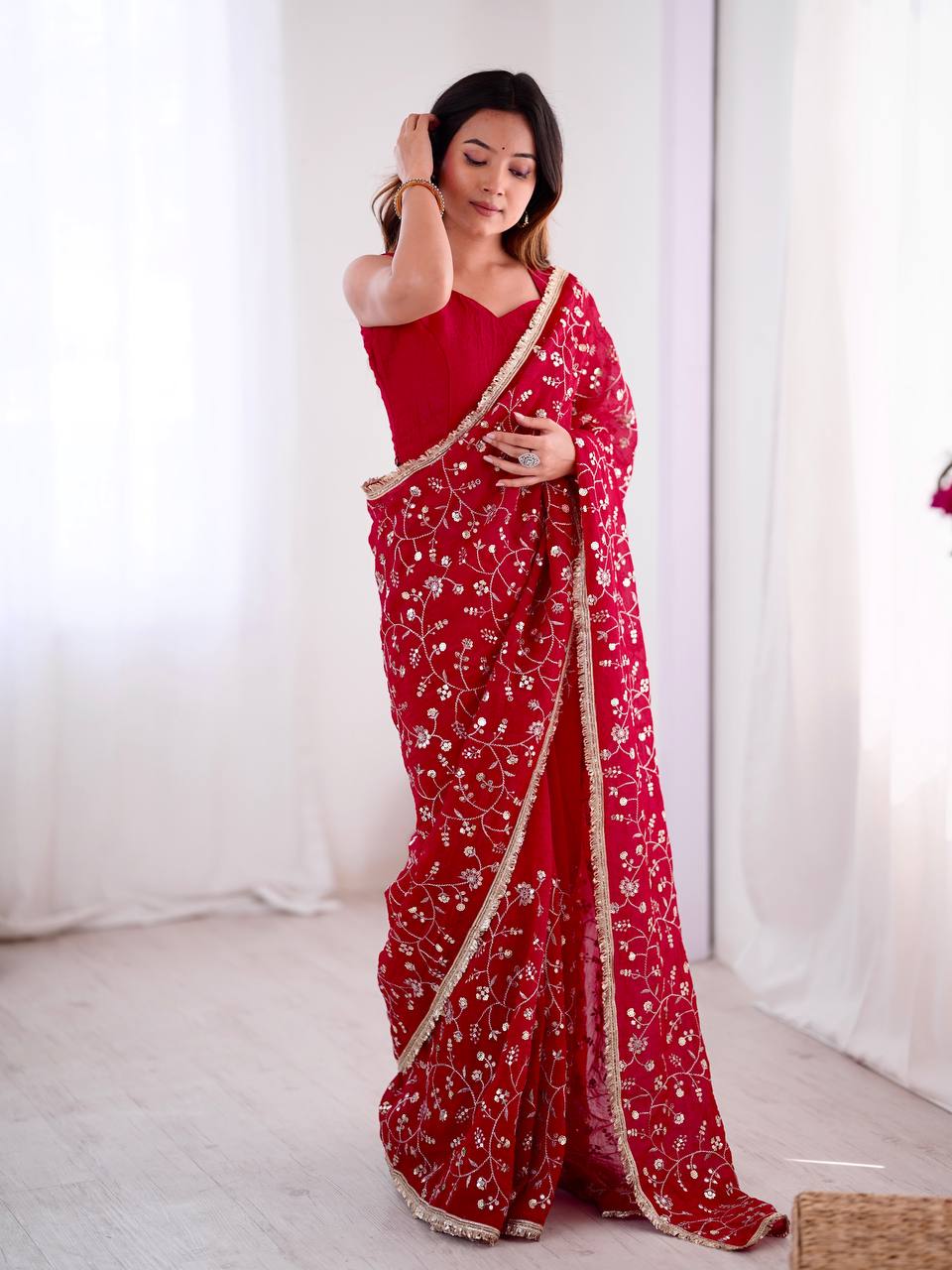 Red embroidered saree with intricate golden floral design and matching blouse, perfect for weddings and festive occasions – model showcasing full look indoors.

Woman wearing an elegant red embroidered saree with golden border, posing indoors with soft white curtains in the background.

