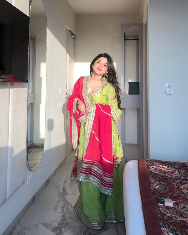 "Smiling woman in lime green sharara suit with sequin detailing and contrasting red dupatta – traditional Indian festive and wedding outfit."

"Lime green sharara set with red dupatta and gota patti work – ethnic festive wear for women"

"Vibrant green and red embroidered sharara suit – perfect for haldi, mehendi, and festive occasions"

"Green sharara suit with red dupatta – festive Indian outfit for women"



